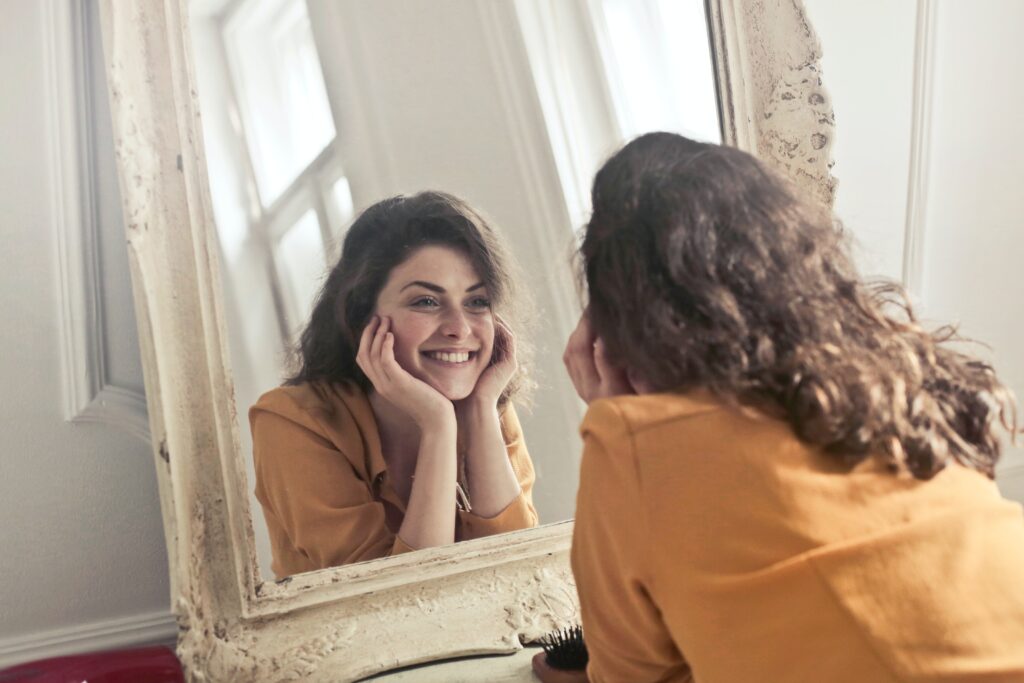 Image d'une femme souriante se regardant dans le miroir tout en réfléchissant à ses objectifs personnels et professionnels.